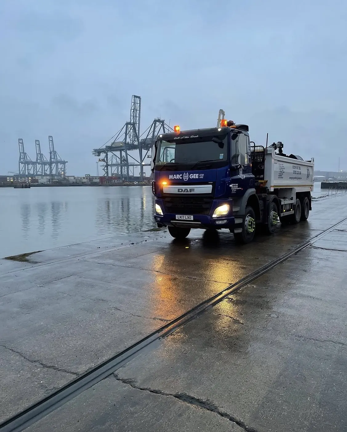 Marc Gee DAF lorry with lights on at the docks at dawn, cranes behind