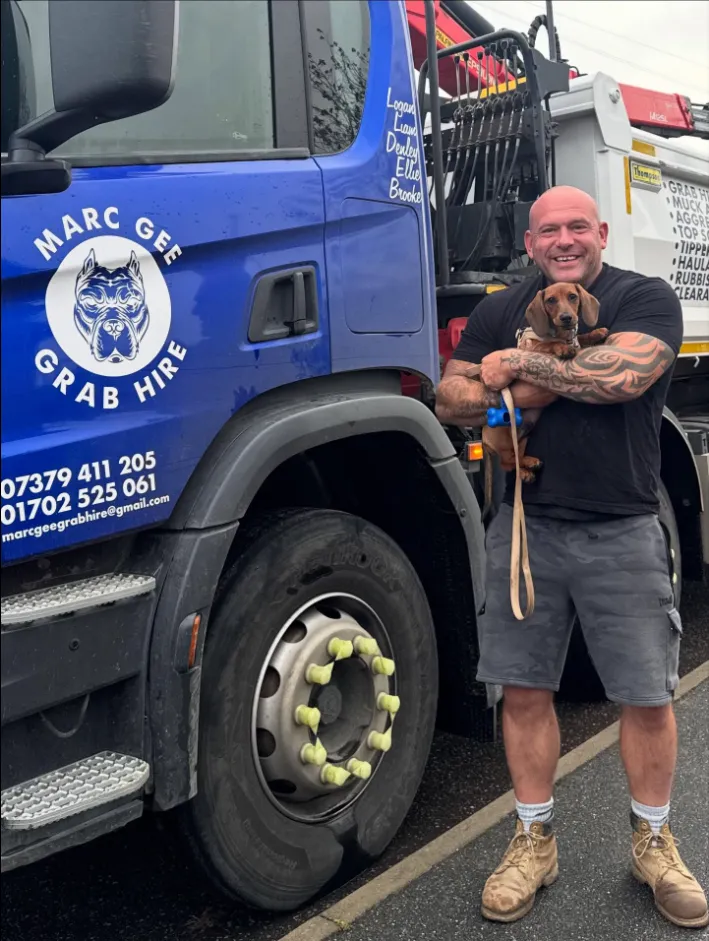 Marc, the owner, holding a small dachshund puppy beside a Marc Gee grab lorry