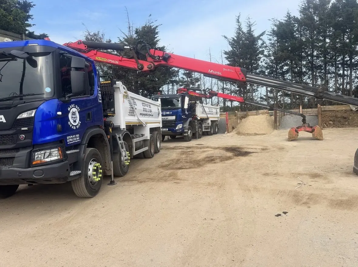 Two Marc Gee grab lorries in the yard with the grab arm extended over sand